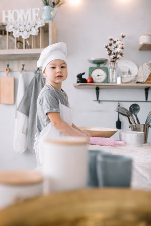 Young boy cute on the kitchen cook chef in white uniform and hat near table. homemade gingerbread. the boy cooked the chocolate cookiesの写真素材