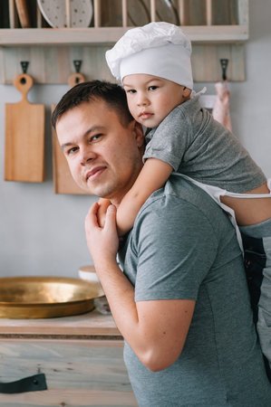 Young man and his son with oven sheet in kitchen. Father with little son on the kitchen.