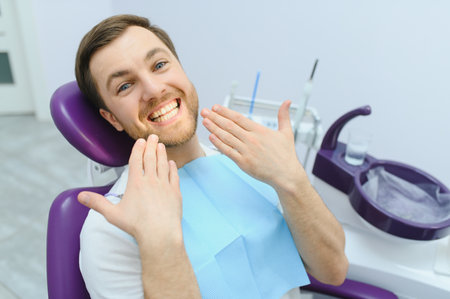 young bearded man sitting in dental chair, visiting modern dental clinic, having regular checkup, woman dentistの写真素材