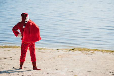 Santa Claus with at big Christmas sack full of gifts stay at ocean tropical sandy beach - X-mas or New Year's travel vacation discounts and travel agencies price reductions conceptの写真素材