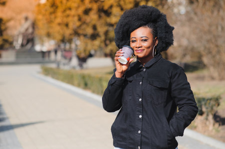 Portrait of a smiling young African American girl with pigtails with coffee walking in the street on a sunny day. outdoor photo.の写真素材