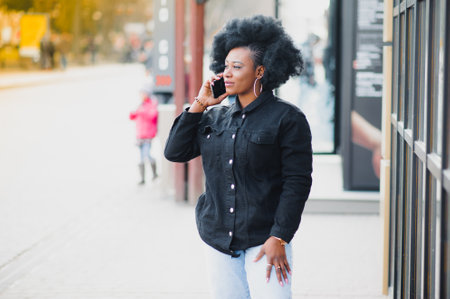 Attractive happy dark-skinned model with Afro hairstyle and nose-ring, posing outdoors against urban...
