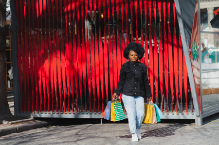 Attractive young African-American woman shopping - shopping bags, outdoors, street view, suitable for holiday shopping themes, among othersの写真素材