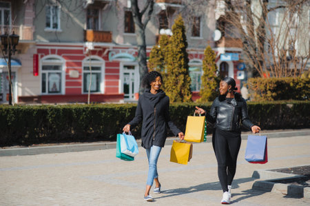 Two afro american women friends in the city on a shopping trip carrying colorful shopping bags.の写真素材