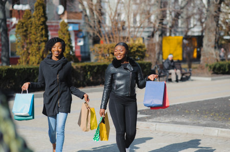 Two afro american women friends in the city on a shopping trip carrying colorful shopping bags.の写真素材