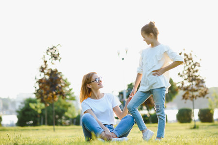 Happy and friendly family in nature. Emotional and young mother hugs her smiling little daughter lying on the grass. summer park. Positive emotions.Childhood. Summertime Lifestyleの写真素材