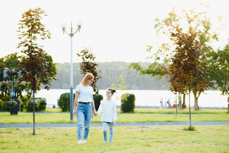 Attractive young woman with her little cute daughter are spending time together outdoors. Mom with daughter in the park on a green grass during the sunset.の写真素材