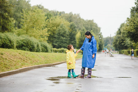 Mother with son walking in the park in the rain wearing rubber bootsの写真素材