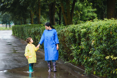 Mother with son walking in the park in the rain wearing rubber bootsの写真素材