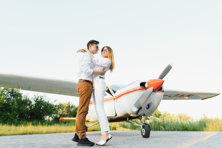Full-length image of beautiful young stylish couple near private plane. Walking on runway in airport in front of airplane.の写真素材