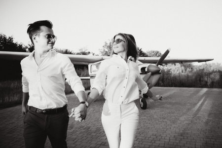 Full-length image of beautiful young stylish couple near private plane. Walking on runway in airport in front of airplane.の写真素材