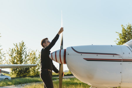 Pensive attractive young man pilot standing near small aircraft