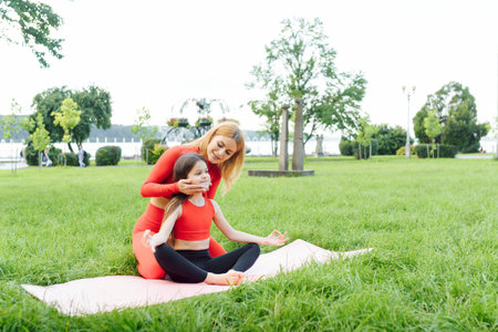 Mother and daughter doing yoga exercises on grass in the park at the day timeの写真素材