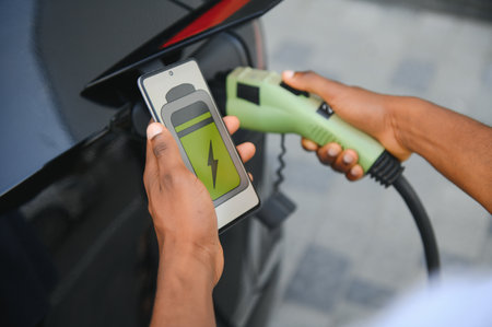 Man holding smartphone while charging car at electric vehicle charging station, closeupの写真素材