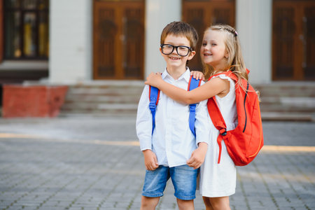 Happy children - boy and girl with books and backpacks on the first school day. Excited to be back to school after vacation. Full length outdoor portrait.の写真素材
