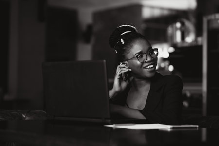 Beautiful Afro American girl in casual clothes is using a laptop and smiling while sitting in cafeの写真素材