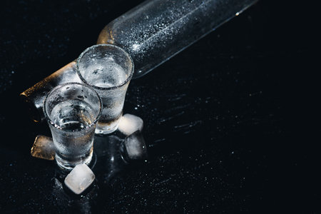 Close-up view of bottle of vodka with glasses standing on ice on black