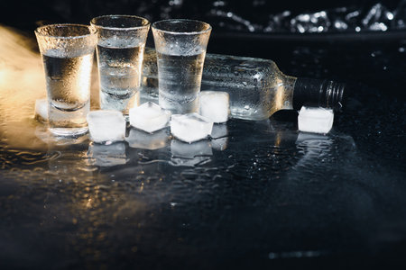 Close-up view of bottle of vodka with glasses standing on ice on black