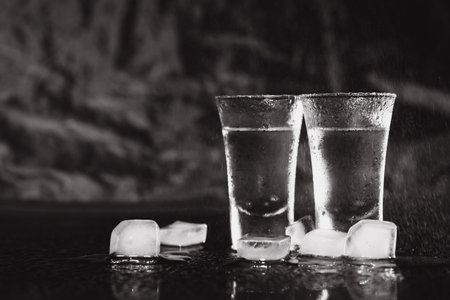 Vodka shots with ice on black table, copy space