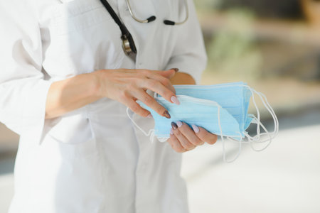 Beautiful doctor holding protective mask in hand, happy to end quarantine. copy space, white...
