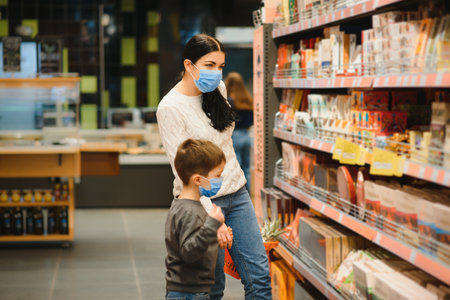 Young woman and her kid wearing protective face masks shop a food at a supermarket during the coronavirus epidemic or flu outbreakの写真素材