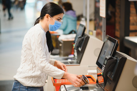 young beautiful girl in medical mask against coronavirus at checkout in supermarket.の写真素材
