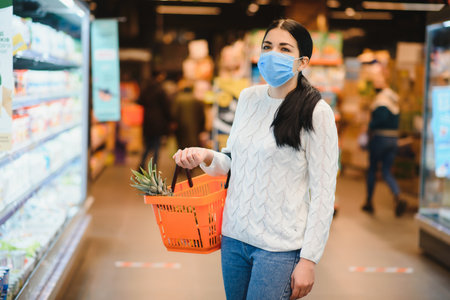 Alarmed female wears medical mask against coronavirus while grocery shopping in supermarket or storeの写真素材