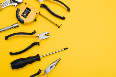 Yellow and black handy tools (pilers and screwdriver) isolated on yellow background