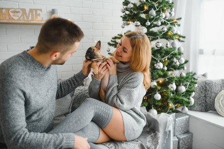 Merry Christmas and Happy New Year. Young beautiful couple are playing with their dog in the festive New Year living room just before the Christmas.の写真素材