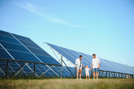 A wide shot of a happy family standing together and smiling at camera with a large solar panel in...