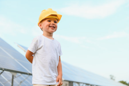 A happy little boy in a yellow helmet is standing on a solar panel farmの写真素材