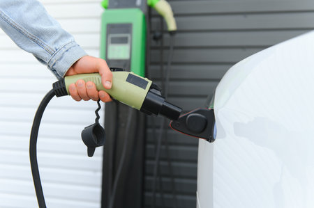 young handsome man holding charging cable at electric charging station point standing near his new car.の写真素材