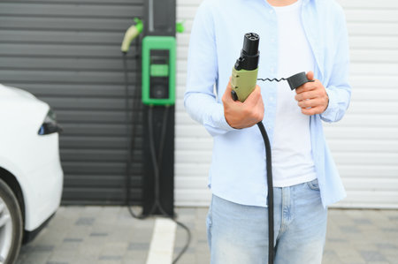 Man holding power supply cable at electric vehicle charging station. Close-up.の写真素材