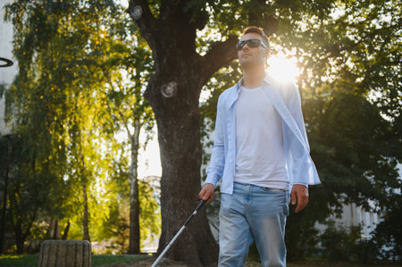 Young handsome blinded man walking with stick in town.の写真素材
