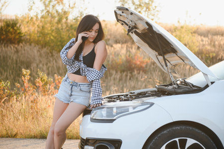 The young girl broke the car and she opened the hood and tried to repair the car on the road. A...
