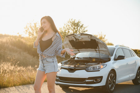 Women talking on the phone about problem with her car she can't. Young sexy girl consults on the phone during car repair. open the hood of the gray car.の写真素材