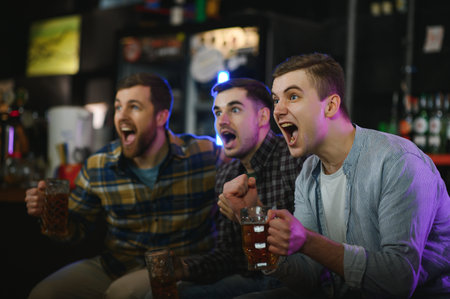 Sport, people, leisure, friendship, entertainment concept - happy male football fans or good yuong friends drinking beer, celebrating victory at bar or pub. Human positive emotions concept.の写真素材