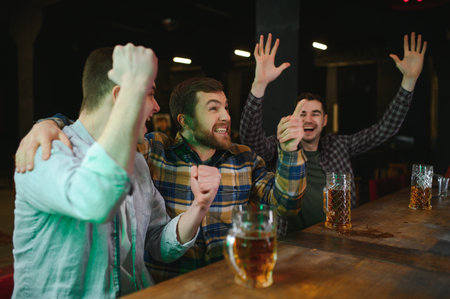 Soccer fans cheering for favorite team while enjoying drinks. Group of supporters celebrating victory while watching football match on TV in a club. Happy friends shouting while cheering for a goalの写真素材