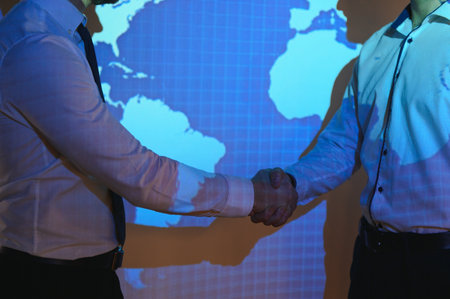 Handshake with map of the world in background. two businessmen on the background of the world map shake hands, the concept of international relations.の写真素材