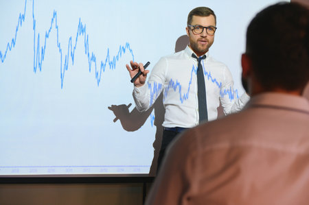 Trading teaching. Male leader talking to employees, showing the plan on the projector in office of...