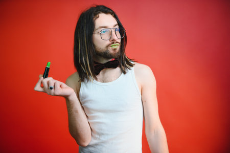 Young man applying lip gloss on his lips and looking in camera like mirror. Gay man doing make up...