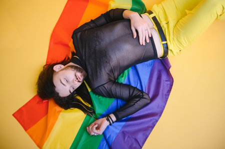Gay man hold rainbow striped flag isolated on colored background studio portrait. People lifestyle...
