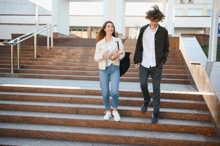 Two happy students walking towards camera and talking in a university campus