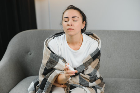 Nasal spray in hand of sick young woman sitting on couch. Allergic rhinitis symptoms and treatment.の写真素材