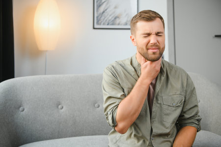 Sore throat, men with pain in neck in home interior, health problems concept.の写真素材