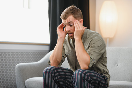 Ill man sitting on his bed with his head on his hand.の写真素材