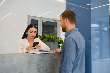 Nice friendly woman talking to the client while standing at the receptionの写真素材