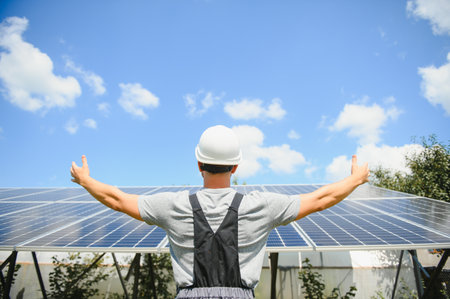 Smiling worker with solar station, raising his hands, showing thumbs up on a background of...