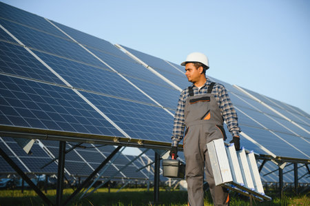 Male arabian engineer in helmet and brown overalls checking resistance in solar panels outdoors....