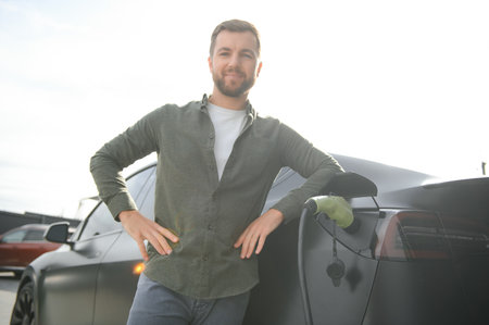Full length portrait of young handsome bearded man in casual wear, standing at the charging station...